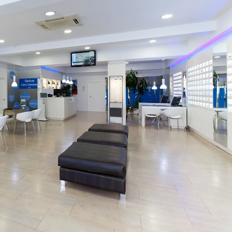 Interior de la óptica de Gran Vía 49: suelo claro, bancos de espera, mostrador al fondo y la luz azul del techo